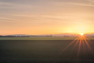 Prairie farmland under an orange sunset sky