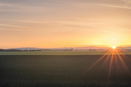Prairie farmland under an orange sunset sky