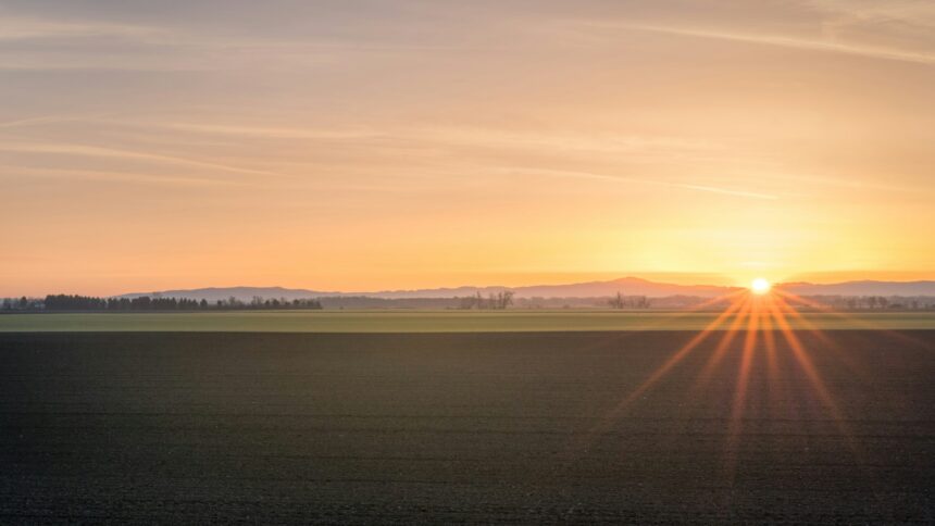 Prairie farmland under an orange sunset sky