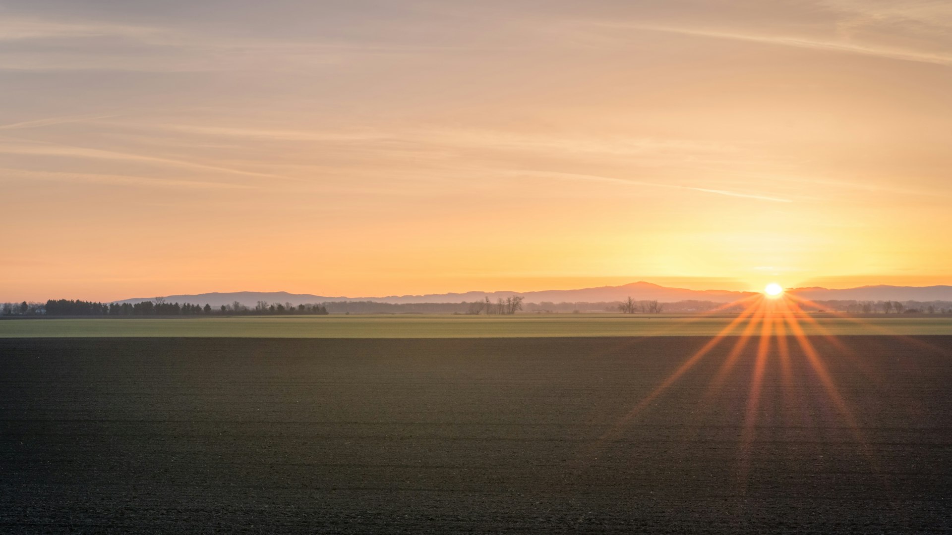 Prairie farmland under an orange sunset sky