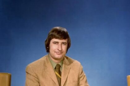 Ralph Klein in a studio portrait from his years as a Calgary television reporter, tan jacket against a blue backdrop