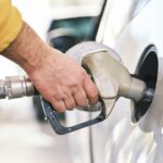 A hand holding a fuel nozzle in a vehicle filler neck