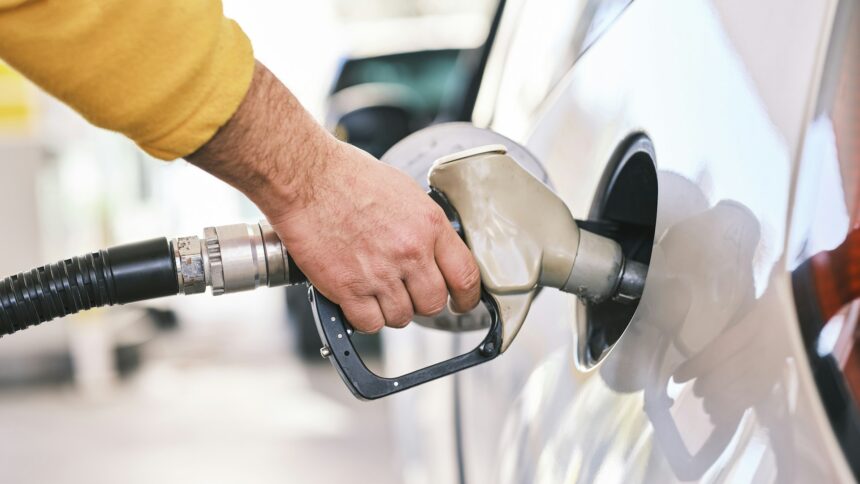 A hand holding a fuel nozzle in a vehicle filler neck