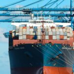 Shipping containers stacked beside gantry cranes at a port