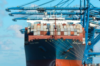 Shipping containers stacked beside gantry cranes at a port