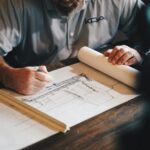 Hands drafting house plans on a desk with a scale ruler