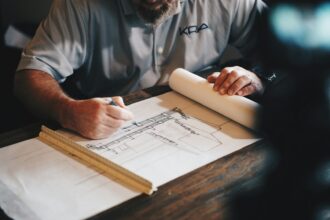 Hands drafting house plans on a desk with a scale ruler