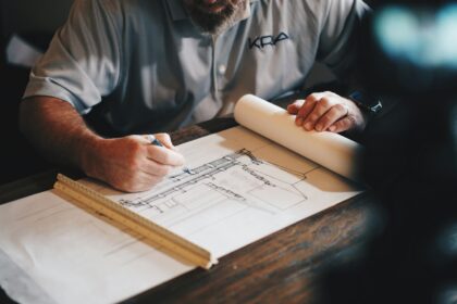 Hands drafting house plans on a desk with a scale ruler