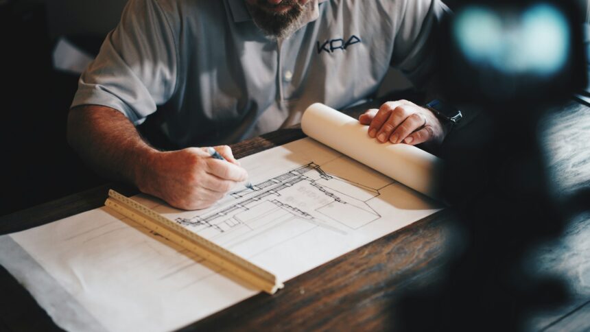 Hands drafting house plans on a desk with a scale ruler