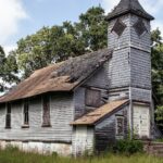 A small white wooden country church standing among trees