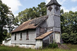 A small white wooden country church standing among trees