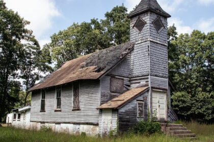 A small white wooden country church standing among trees