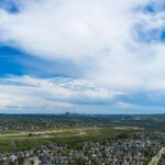 Aerial view of Calgary suburban neighbourhoods stretching toward the downtown skyline under summer clouds