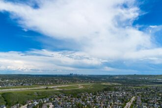 Aerial view of Calgary suburban neighbourhoods stretching toward the downtown skyline under summer clouds