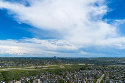 Aerial view of Calgary suburban neighbourhoods stretching toward the downtown skyline under summer clouds