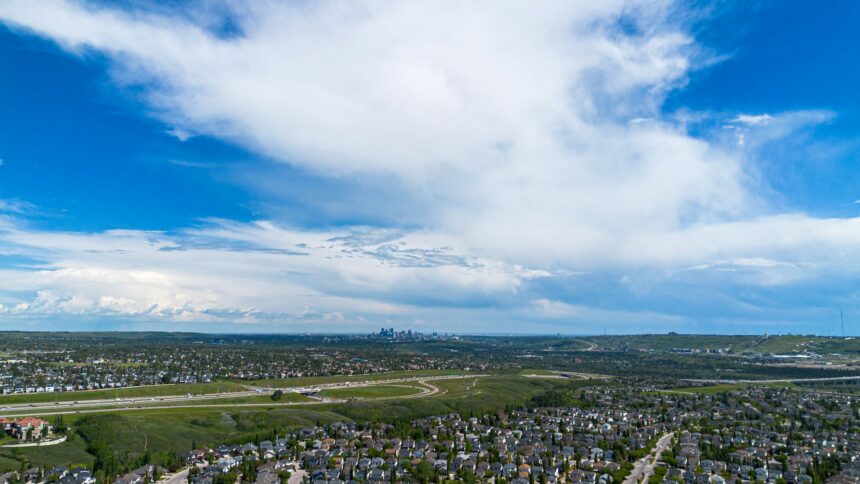 Aerial view of Calgary suburban neighbourhoods stretching toward the downtown skyline under summer clouds