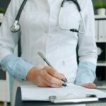 A physician writing notes on a clipboard, the paperwork the Health Innovation Lab targets first