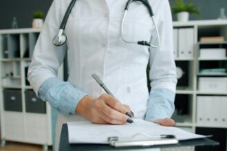 A physician writing notes on a clipboard, the paperwork the Health Innovation Lab targets first
