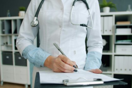 A physician writing notes on a clipboard, the paperwork the Health Innovation Lab targets first