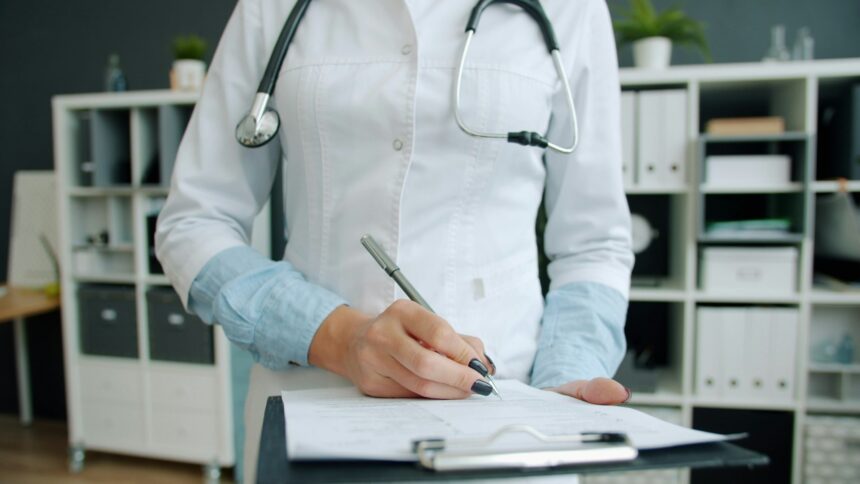 A physician writing notes on a clipboard, the paperwork the Health Innovation Lab targets first