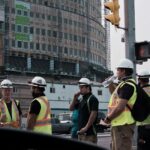Construction workers in hard hats and safety vests beside a building site