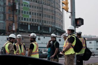 Construction workers in hard hats and safety vests beside a building site
