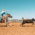 A rider on horseback swinging a lasso in a rodeo arena