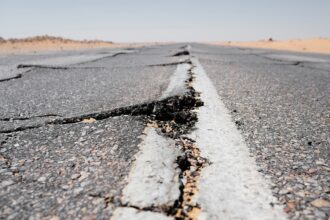 A deep crack running across a worn highway and its centre line