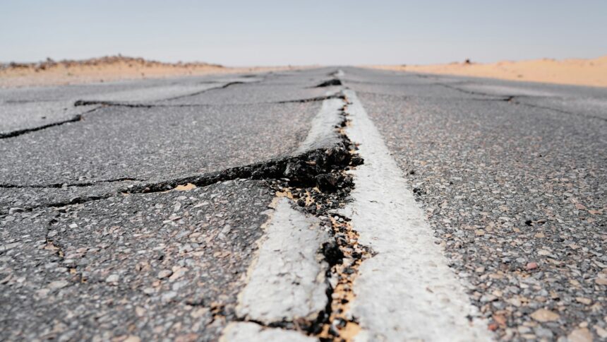 A deep crack running across a worn highway and its centre line