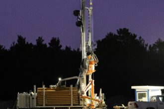 A drilling rig lit up and operating after dark on a well site