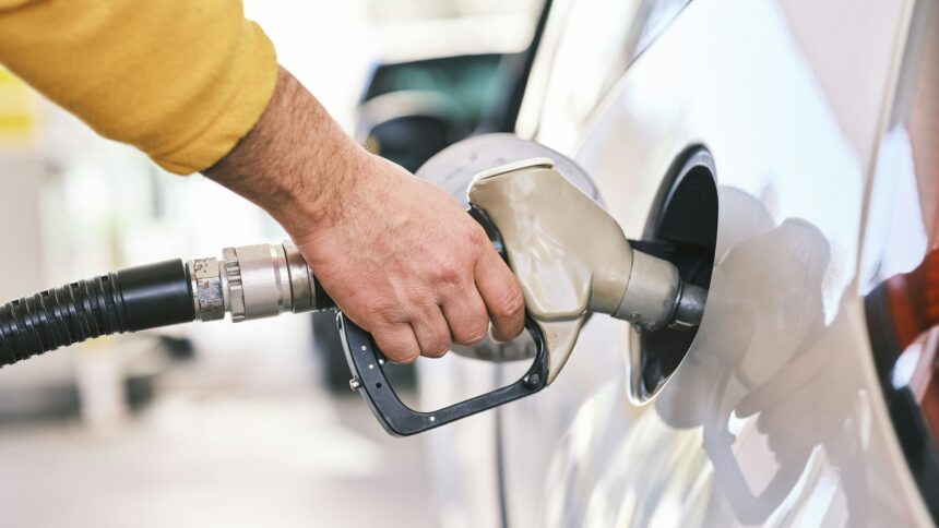 Hand holding a fuel nozzle in the open tank of a white car at a gas station