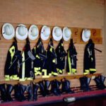 Firefighter turnout gear and helmets hanging on a fire hall wall