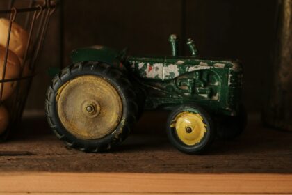 A green toy tractor standing on a wooden shelf