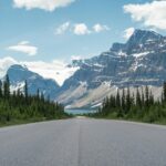 Paved two-lane road running toward a glaciated peak and a blue lake on the Icefields Parkway in the Canadian Rockies
