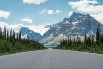 Paved two-lane road running toward a glaciated peak and a blue lake on the Icefields Parkway in the Canadian Rockies