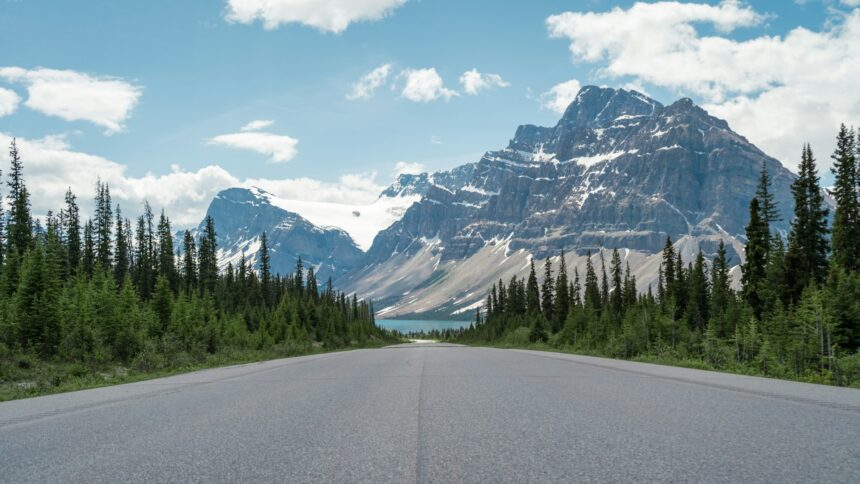 Paved two-lane road running toward a glaciated peak and a blue lake on the Icefields Parkway in the Canadian Rockies