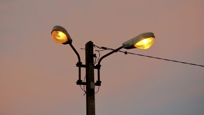 Two old street lamps glowing against an evening sky