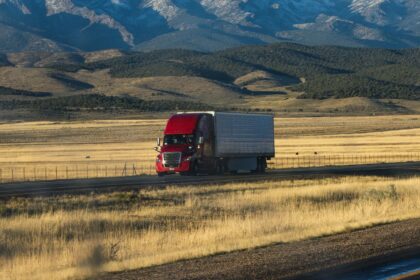 A red semi truck crossing golden grassland below rolling hills