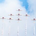 Nine red and white jets flying in tight formation trailing white smoke