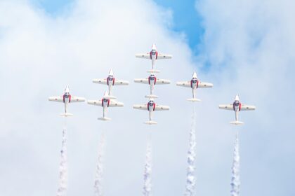 Nine red and white jets flying in tight formation trailing white smoke