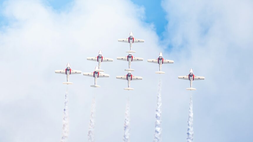 Nine red and white jets flying in tight formation trailing white smoke