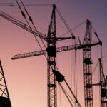 Tower cranes silhouetted against a pink evening sky