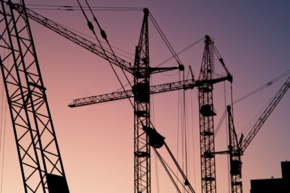 Tower cranes silhouetted against a pink evening sky