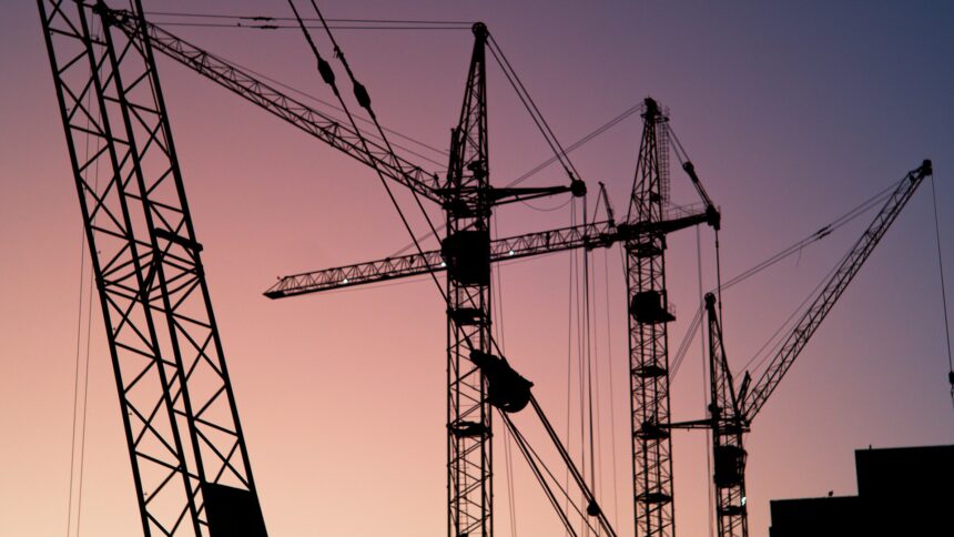Tower cranes silhouetted against a pink evening sky