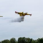 Two yellow water bomber aircraft releasing water over a hillside