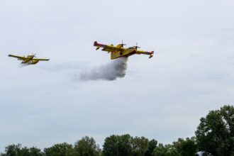 Two yellow water bomber aircraft releasing water over a hillside