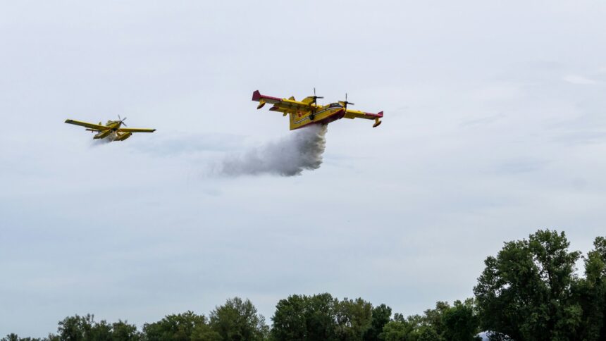 Two yellow water bomber aircraft releasing water over a hillside