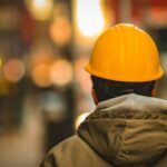 A worker in an orange hard hat and work jacket seen from behind