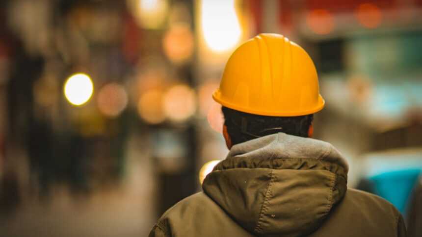 A worker in an orange hard hat and work jacket seen from behind
