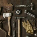 Worn hand tools and leather work gloves laid out on a wooden bench